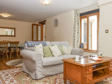 A living room with a sofa cushions and a wooden coffee table near a window and dining table with chairs at Peace Cottage in Queens Nympton near South Molton