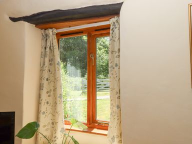 A wooden framed window with floral curtains and a green plant by the sill at Peace Cottage in Queens Nympton near South Molton