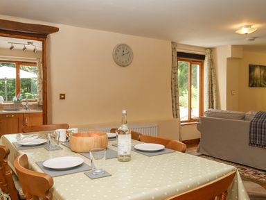 A dining table set with plates and glasses next to a living room with a sofa at Peace Cottage in Queens Nympton near South Molton