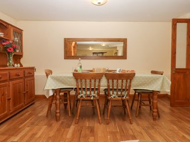 A dining room with a wooden table and six chairs a sideboard with flowers and a mirror on the wall at Peace Cottage in Queens Nympton near South Molton