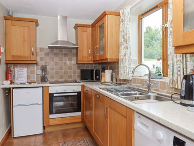 A kitchen with wooden cabinets a sink a microwave an oven a fridge and a window at Peace Cottage Queens Nympton near South Molton