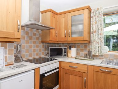 A kitchen with wooden cabinets a microwave an oven and stovetop a sink and utensils at Peace Cottage Queens Nympton near South Molton