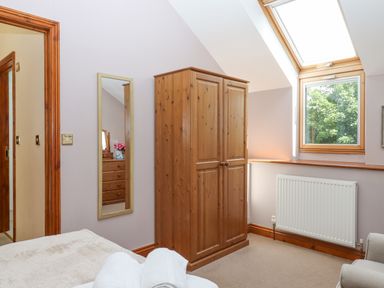 A bedroom with a wooden wardrobe a wall mirror a skylight window and a radiator at Peace Cottage in Queens Nympton near South Molton