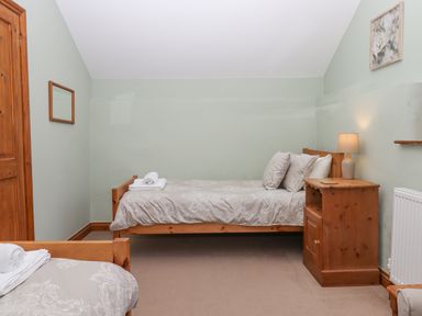 A bedroom with two wooden single beds a bedside table with a lamp a wooden door a wall mirror and a framed picture at Peace Cottage Queens Nympton near South Molton
