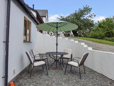 An outdoor seating area with four chairs a round table and a green umbrella next to a white building at Peace Cottage in Queens Nympton near South Molton