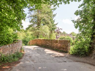 A narrow stone bridge over a dirt road surrounded by trees and bushes at Peace Cottage in Queens Nympton near South Molton