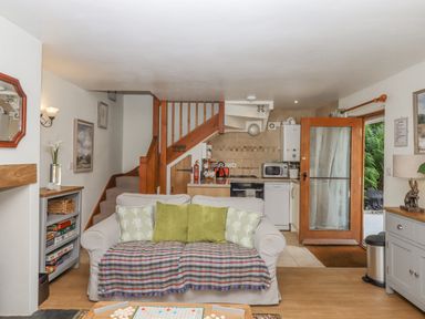 A living room with a sofa and pillows in front of a staircase next to a kitchen and wooden door at Dove Cottage in Queens Nympton near South Molton