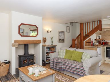 A living room with a sofa with green pillows a wood burning stove and a coffee table with a scrabble game at Dove Cottage Queens Nympton near South Molton