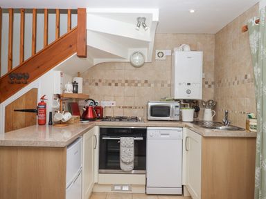 A kitchen with a stove oven dishwasher microwave kettle sink and fire extinguisher under wooden stairs at Dove Cottage Queens Nympton near South Molton
