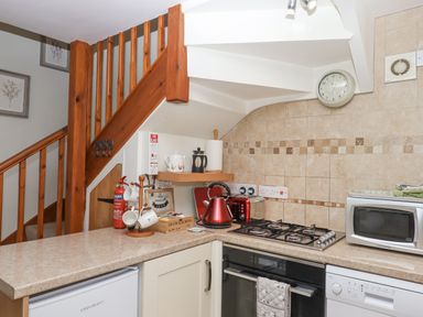 A kitchen with wooden stairs a stove kettle microwave and countertop at Dove Cottage Queens Nympton near South Molton