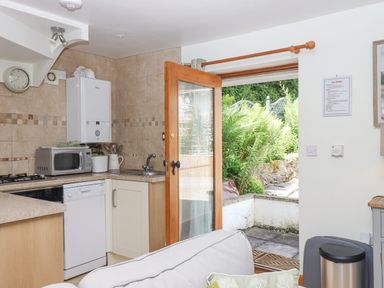 A kitchen with a microwave dishwasher sink and open wooden door leading to a garden at Dove Cottage in Queens Nympton near South Molton