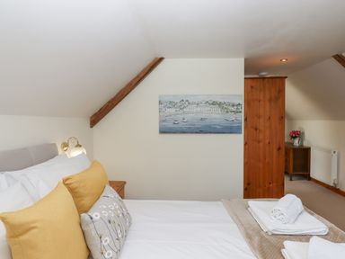 A bedroom with a bed with yellow and floral pillows a wooden wardrobe and a painting on the wall at Dove Cottage in Queens Nympton near South Molton