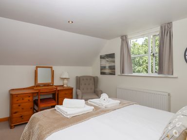 A bedroom with a bed with towels on it a wooden dressing table with a mirror a lamp an armchair and a window with curtains at Dove Cottage Queens Nympton near South Molton