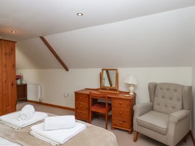 A bedroom with a wooden desk and chair a beige armchair and folded towels on a bed at Dove Cottage Queens Nympton near South Molton
