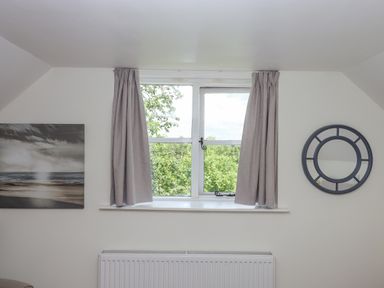 A window with gray curtains between a round mirror and a landscape painting above a radiator at Dove Cottage Queens Nympton near South Molton