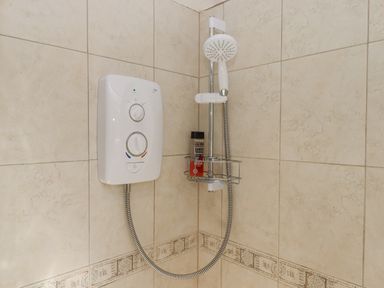 A tiled shower corner with an electric shower unit and a handheld shower head at Dove Cottage Queens Nympton near South Molton