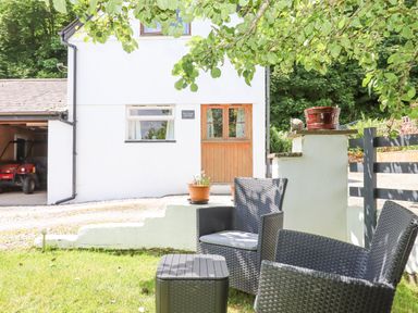 A white house with wooden door and window near black patio chairs and table on grass at Dove Cottage Queens Nympton near South Molton