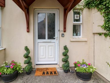A front door with a doormat and two spiral topiary plants and flower pots on either side at 23 Cois Caol in Skibbereen County Cork