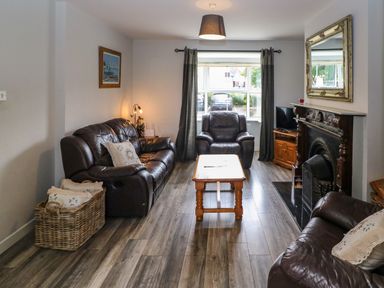 A living room with leather sofas a wooden coffee table a fireplace and a window with curtains at 23 Cois Caol in Skibbereen County Cork