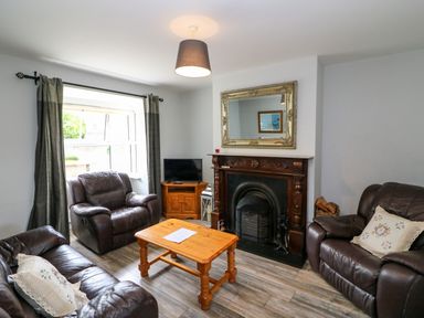 A living room with dark leather sofas a wooden coffee table a fireplace and a TV in the corner at 23 Cois Caol in Skibbereen County Cork