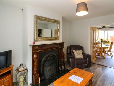 A living room with a wooden fireplace and mirror leather armchair and wooden table with papers at 23 Cois Caol in Skibbereen County Cork