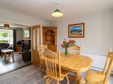 A dining room with a wooden table and chairs a vase with flowers on the table a framed picture on the wall and a wooden corner cabinet at 23 Cois Caol in Skibbereen County Cork