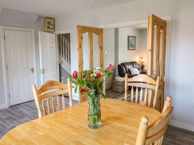A wooden dining table with four chairs and a vase of flowers in a room with open wooden doors leading to a living area at 23 Cois Caol in Skibbereen County Cork