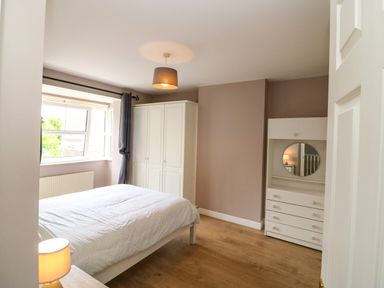 A bedroom with a bed a wardrobe a chest of drawers with a round mirror and a window at 23 Cois Caol in Skibbereen County Cork