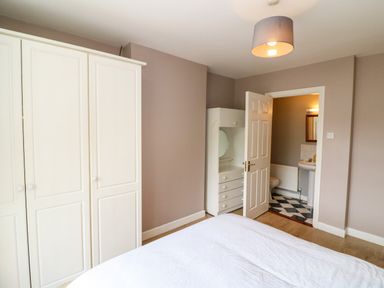 A bedroom with a white wardrobe a dresser with a round mirror a bed and an open door leading to a bathroom at 23 Cois Caol in Skibbereen County Cork