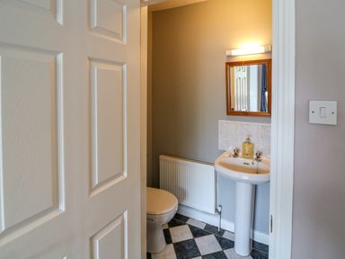 A small bathroom with a toilet, pedestal sink, mirror with light, and radiator at 23 Cois Caol in Skibbereen County Cork