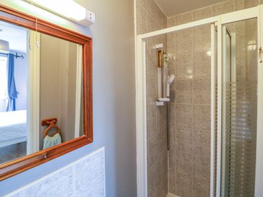 A bathroom with a tiled shower enclosure a wooden framed mirror and a towel ring visible through the mirror at 23 Cois Caol in Skibbereen County Cork