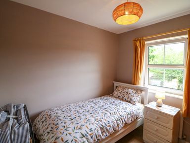 A bedroom with a single bed beside a window with a bedside table and lamp at 23 Cois Caol in Skibbereen County Cork