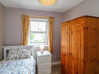 A small bedroom with a single bed a bedside table with a lamp and a wooden wardrobe at 23 Cois Caol in Skibbereen County Cork