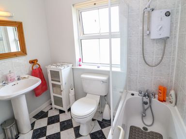 A bathroom with a pedestal sink a toilet a bathtub with shower a small cabinet and a window at 23 Cois Caol in Skibbereen County Cork