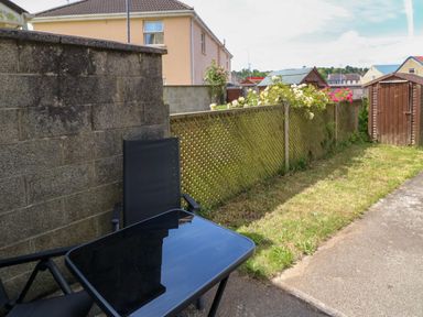 A backyard with a black glass table and chair along a concrete wall and a wooden fence with flowers at 23 Cois Caol in Skibbereen County Cork