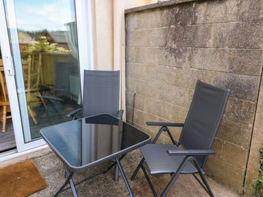 A small outdoor patio area with two black chairs and a square glass table near a sliding glass door at 23 Cois Caol in Skibbereen County Cork
