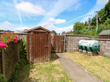 A small garden with a wooden shed a pathway a green water tank and a stone wall at 23 Cois Caol in Skibbereen County Cork