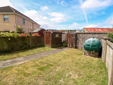 A backyard with grass path garden sheds and a green oil tank at 23 Cois Caol in Skibbereen County Cork