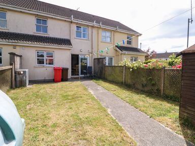 A backyard with a concrete path leading to a house with sliding doors green grass and a clothesline at 23 Cois Caol in Skibbereen County Cork