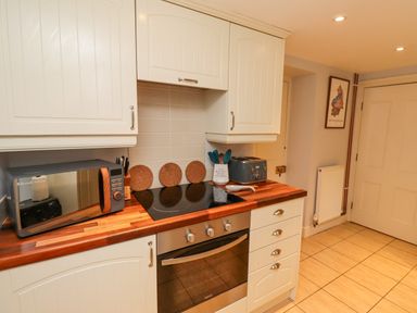 A kitchen with white cabinets a wooden countertop a microwave a stove an oven and a toaster at Woodcutters Cottage in Park Village near Haltwhistle