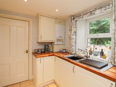 A kitchen corner with cream cabinets wooden countertops a sink under a window and kitchenware on the countertop at Woodcutters Cottage in Park Village near Haltwhistle