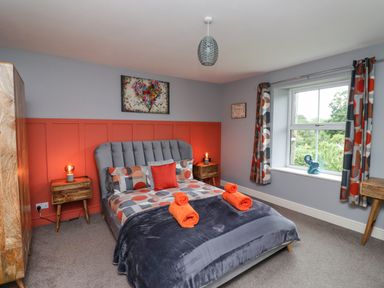 A bedroom with a double bed with patterned bedding two bedside tables two lamps a wooden wardrobe and a window with curtains at Woodcutters Cottage in Park Village near Haltwhistle
