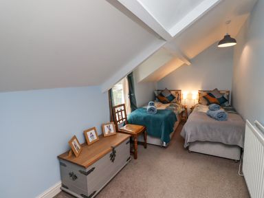A bedroom with two single beds bedside lamps a wooden chair and a chest with framed pictures at Woodcutters Cottage in Park Village near Haltwhistle