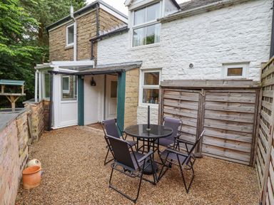 An outdoor patio area with a round table and four chairs on gravel at Woodcutters Cottage in Park Village near Haltwhistle