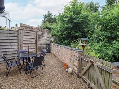 A gravel patio with a round table and four chairs next to a wooden fence and a garden area at Woodcutters Cottage in Park Village near Haltwhistle