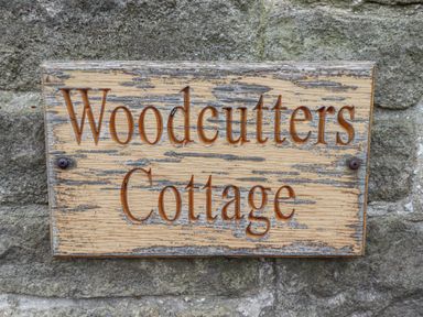 A wooden sign with carved text woodcutters cottage on a stone wall at Woodcutters Cottage in Park Village near Haltwhistle