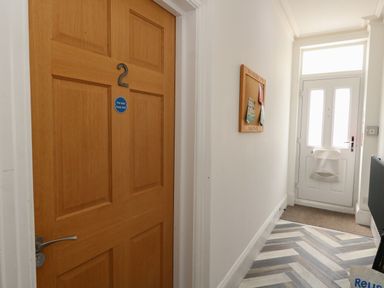 A hallway with a wooden door numbered 2 a notice board on the wall and a white front door at Flat 2 - Studland in Bournemouth