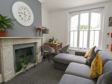 A sitting room with a gray sofa yellow cushions and a marble fireplace with a large wall clock at Flat 2 - Studland in Bournemouth