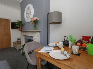 A dining table set with plates holding boiled eggs mugs a teapot and a bowl of fruit near a gray wall and marble fireplace at Flat 2 - Studland in Bournemouth
