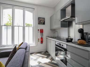 A kitchen with grey cabinets a built in oven a sofa near a large window at Flat 2 - Studland in Bournemouth